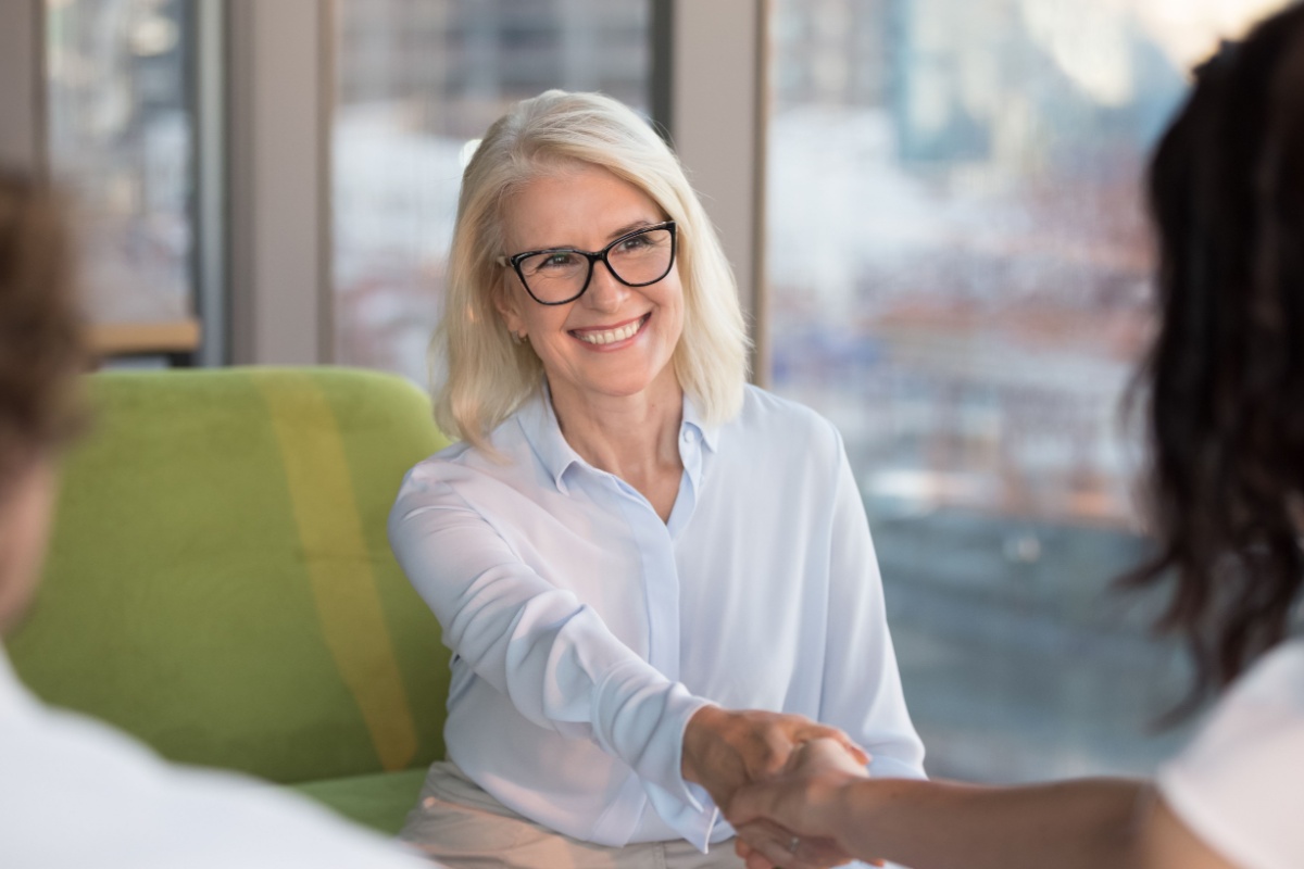 Smiling middle-aged woman shaking hands with another woman