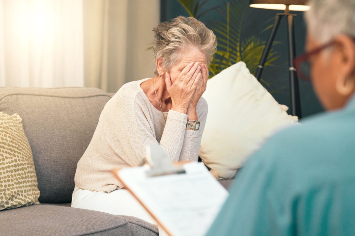 Sad senior woman with her head in her hands talking to a professional